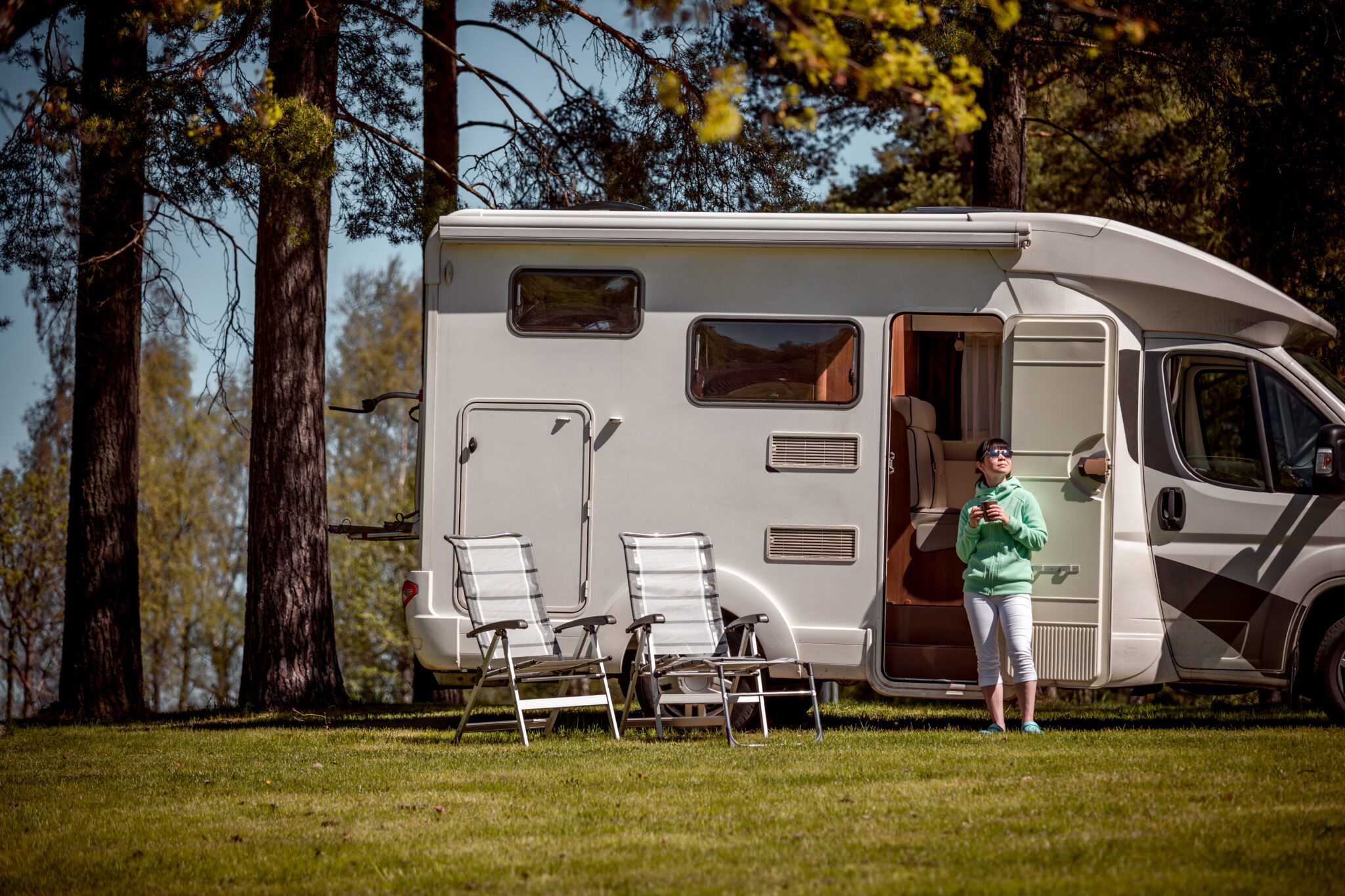 Woman is standing with a mug of coffee near the camper RV.